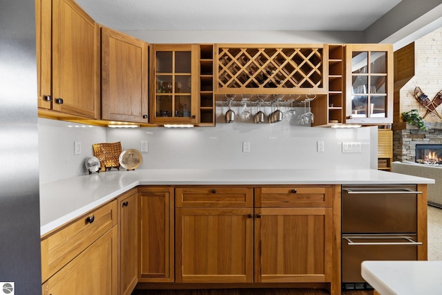 kitchen with glass insert cabinets, brown cabinetry, a fireplace, and light countertops