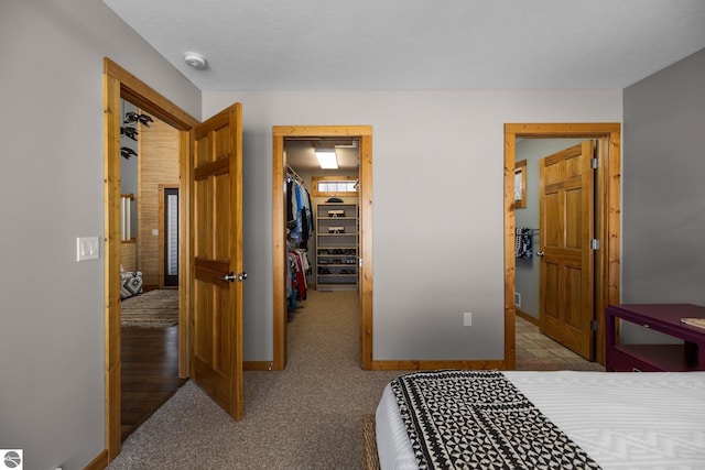 carpeted bedroom featuring a closet, a walk in closet, and baseboards