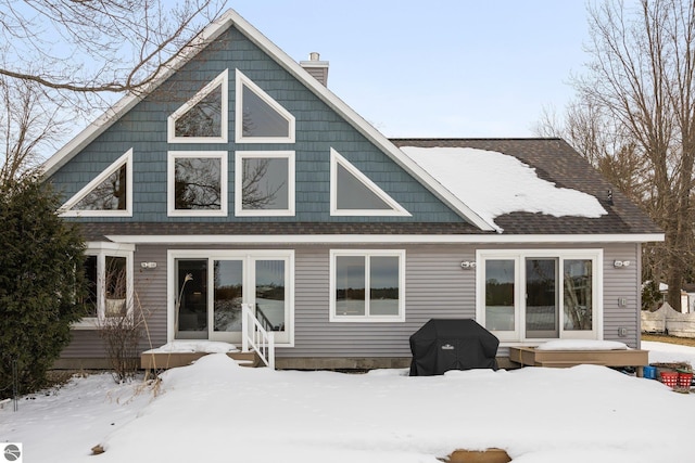 snow covered rear of property with roof with shingles and a chimney