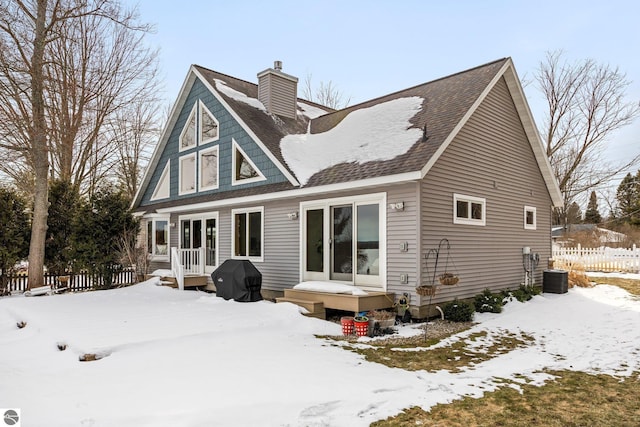 snow covered rear of property featuring cooling unit, a chimney, and fence