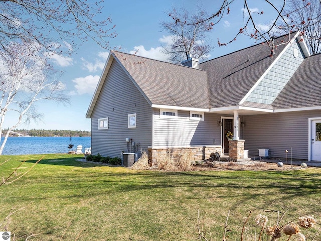 back of property with stone siding, a lawn, a shingled roof, and a water view