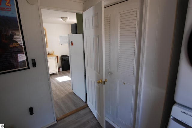 hallway with stacked washer / drying machine and dark wood-style flooring