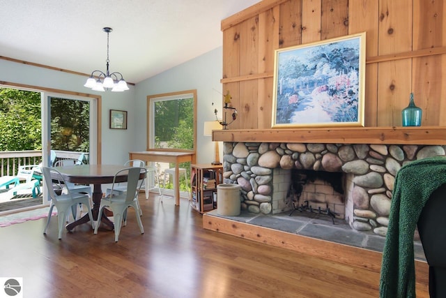 dining area featuring a fireplace, vaulted ceiling, a notable chandelier, and wood finished floors