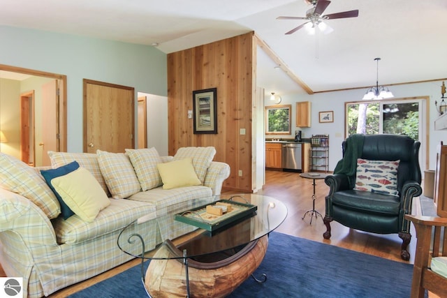 living room with light wood-type flooring, lofted ceiling, wood walls, and ceiling fan with notable chandelier