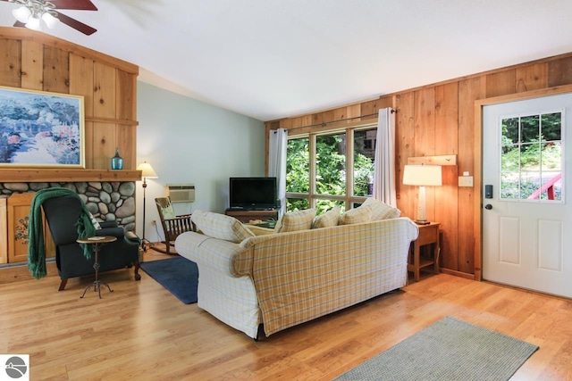 living area featuring light wood finished floors, a fireplace, ceiling fan, vaulted ceiling, and wood walls