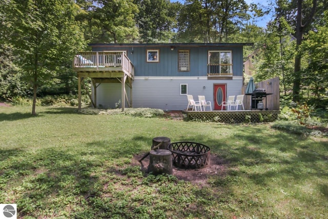 back of property with a wooden deck, a fire pit, and a lawn