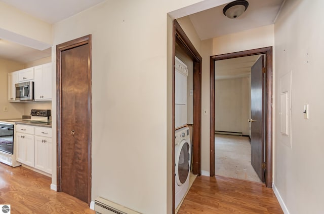 hallway featuring stacked washer and clothes dryer, a baseboard heating unit, light wood-style floors, baseboards, and baseboard heating