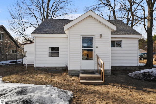 back of house featuring entry steps and roof with shingles