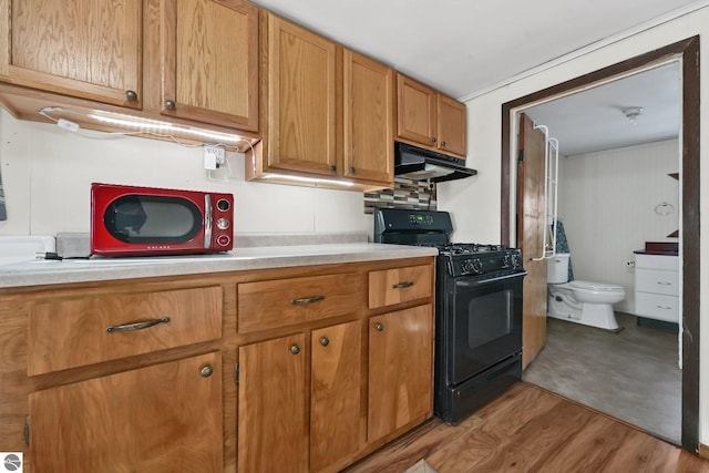 kitchen featuring light wood finished floors, black gas stove, light countertops, under cabinet range hood, and brown cabinets