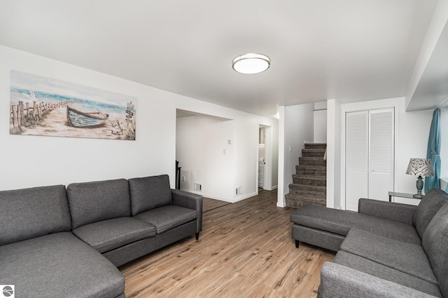 living room featuring stairs, visible vents, baseboards, and light wood-type flooring