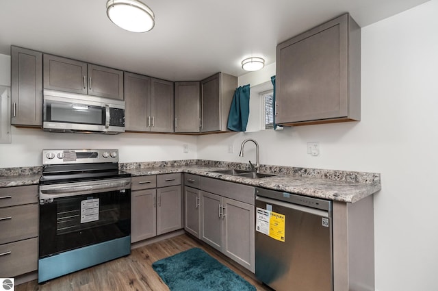 kitchen with a sink, gray cabinets, light wood-type flooring, and stainless steel appliances