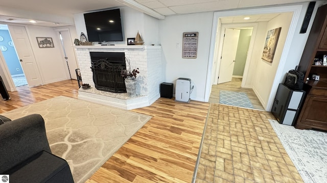 living area with a drop ceiling, recessed lighting, light wood-style floors, baseboards, and a brick fireplace