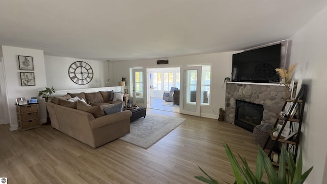 living area with a stone fireplace, light wood-style flooring, and visible vents