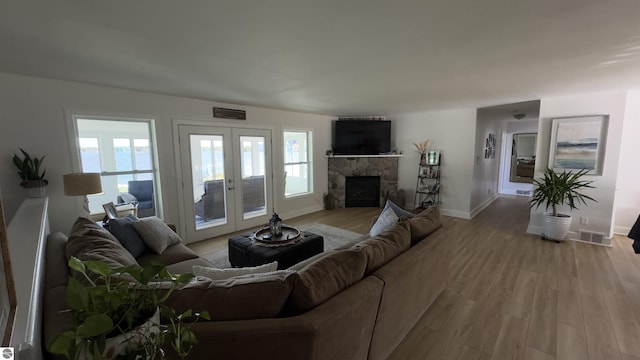 living room featuring visible vents, baseboards, light wood-style flooring, a fireplace, and french doors