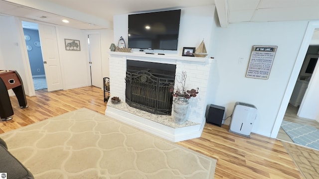 living area with recessed lighting, a fireplace with raised hearth, and wood finished floors