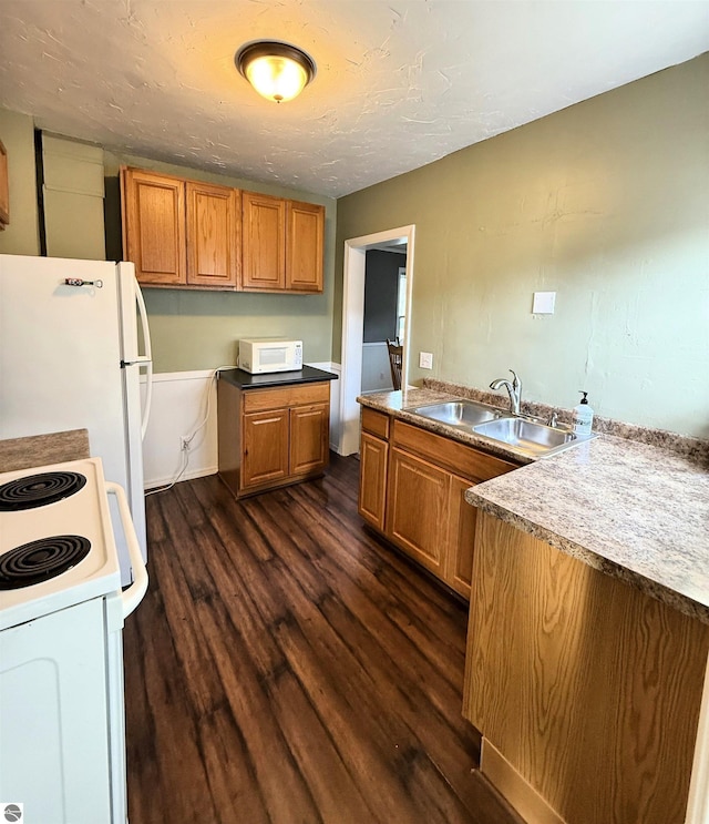 kitchen featuring dark wood-style floors, brown cabinets, white appliances, and a sink