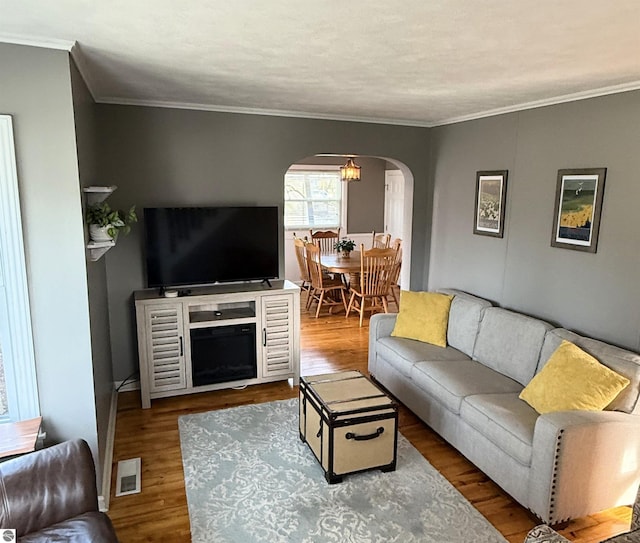 living room with visible vents, arched walkways, wood finished floors, and crown molding