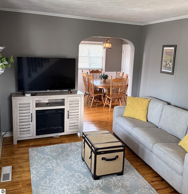 living area featuring wood finished floors, visible vents, arched walkways, ornamental molding, and a chandelier