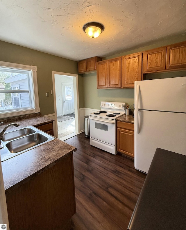 kitchen with white appliances, dark wood finished floors, a sink, dark countertops, and brown cabinets