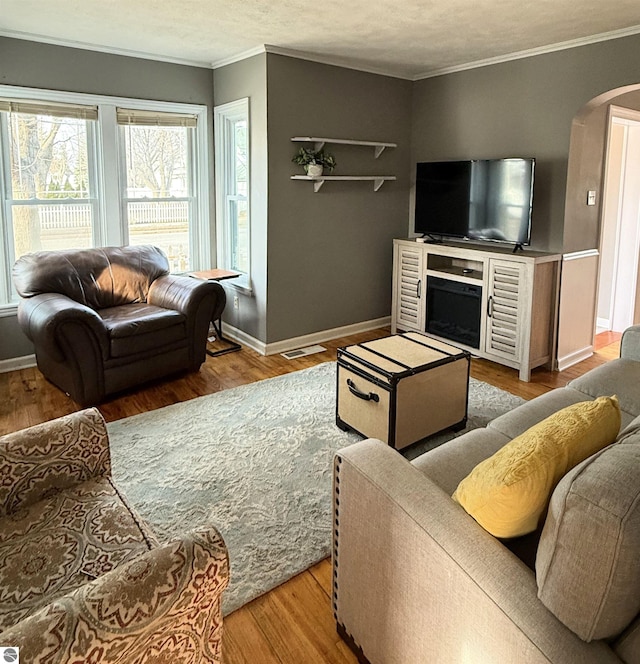 living area featuring arched walkways, crown molding, baseboards, and wood finished floors