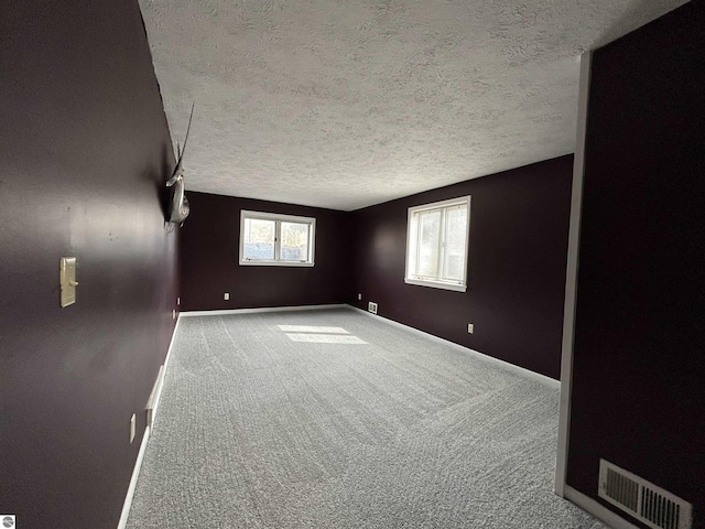 carpeted spare room with baseboards, visible vents, and a textured ceiling