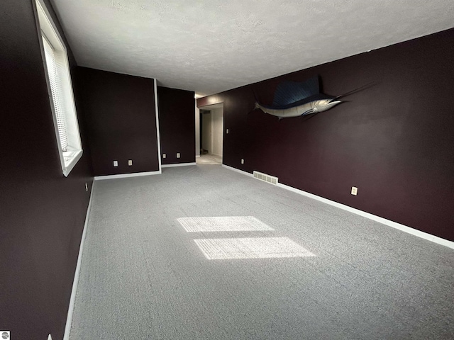 carpeted empty room with visible vents, a textured ceiling, and baseboards