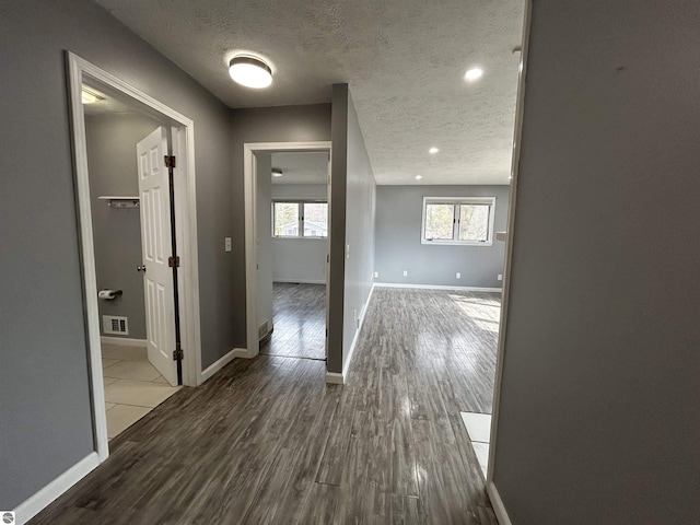 hallway featuring baseboards, wood finished floors, visible vents, and a textured ceiling