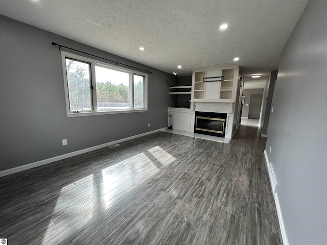 unfurnished living room with a fireplace with flush hearth, a textured ceiling, dark wood-type flooring, and baseboards