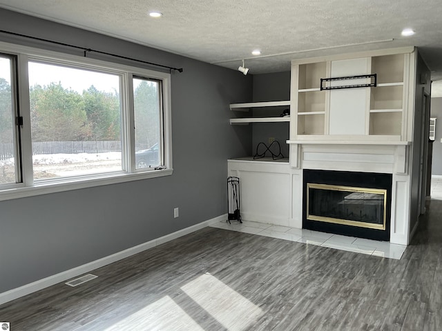 unfurnished living room featuring a glass covered fireplace, wood finished floors, baseboards, and a textured ceiling