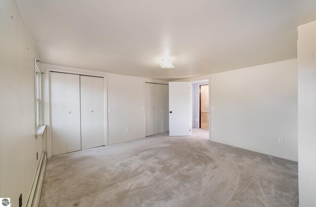 unfurnished bedroom featuring light carpet, baseboard heating, and two closets