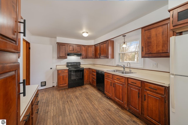 kitchen with a sink, under cabinet range hood, light countertops, black appliances, and dark wood-style flooring