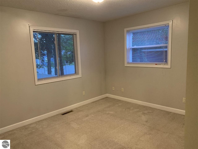 empty room featuring baseboards, visible vents, a textured ceiling, and carpet