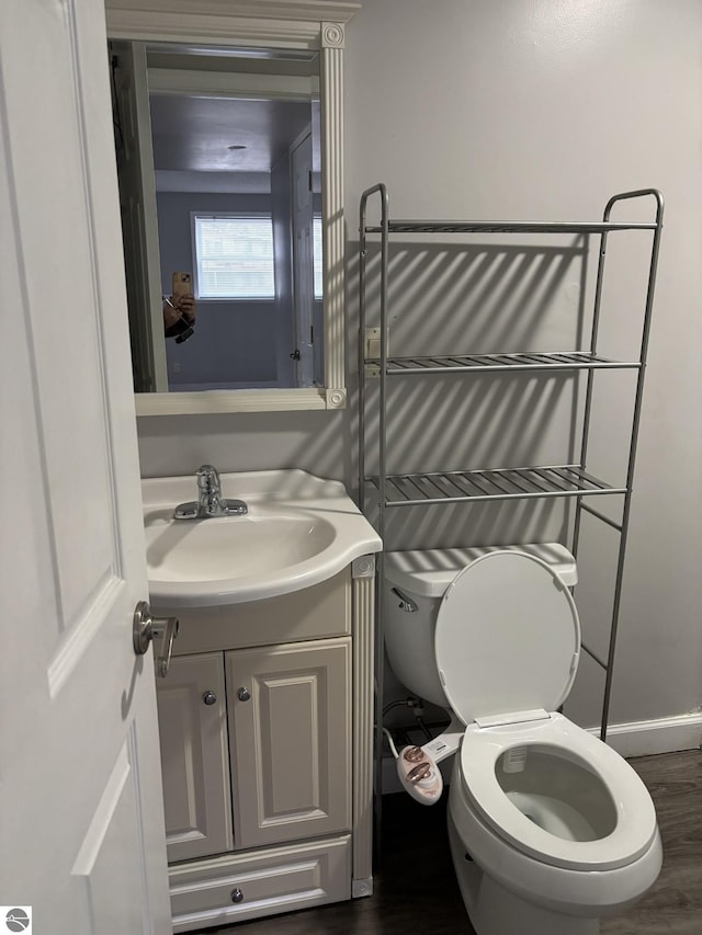 half bath with toilet, vanity, and wood finished floors