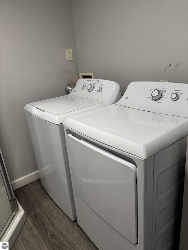 clothes washing area featuring washing machine and clothes dryer, laundry area, baseboards, and wood finished floors