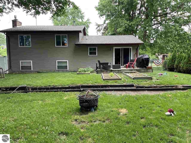 back of house with a vegetable garden, a lawn, a chimney, and an outdoor fire pit