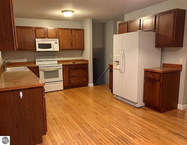 kitchen with white appliances, brown cabinetry, light wood-style flooring, a sink, and a textured ceiling