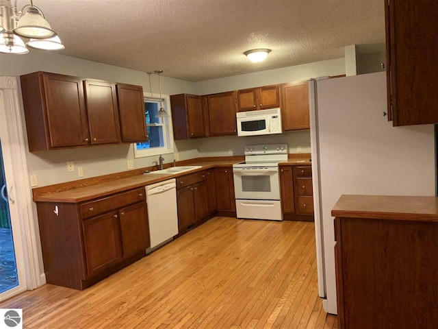 kitchen with a sink, white appliances, light wood-style floors, and pendant lighting