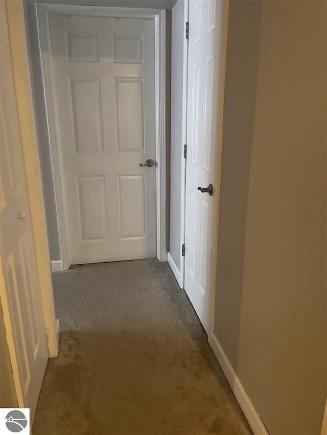 hallway featuring baseboards and dark colored carpet