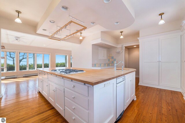 kitchen with butcher block counters, light wood-type flooring, an island with sink, white cabinets, and a sink