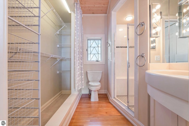 full bathroom with toilet, a stall shower, a sink, wood finished floors, and baseboards