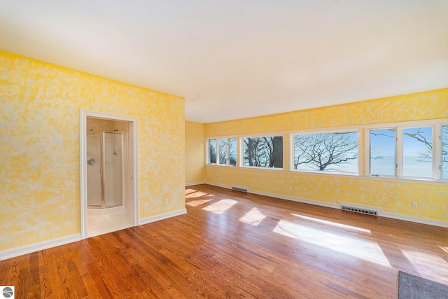 empty room featuring visible vents, baseboards, wood finished floors, and wallpapered walls