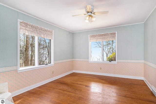 unfurnished room with wallpapered walls, crown molding, baseboards, a wainscoted wall, and hardwood / wood-style floors