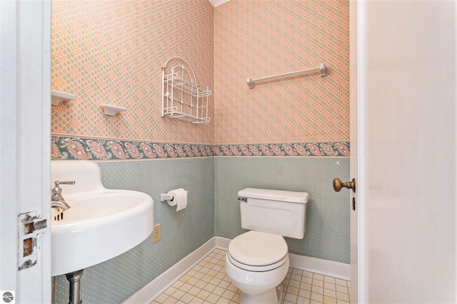 half bath featuring baseboards, wallpapered walls, a sink, tile patterned floors, and toilet