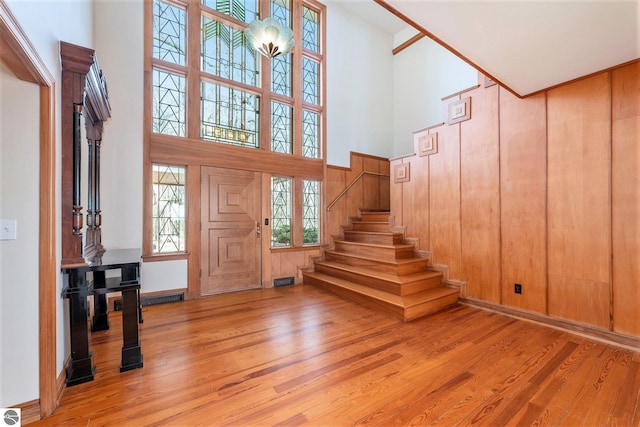 foyer with light wood finished floors, visible vents, wooden walls, stairs, and a high ceiling
