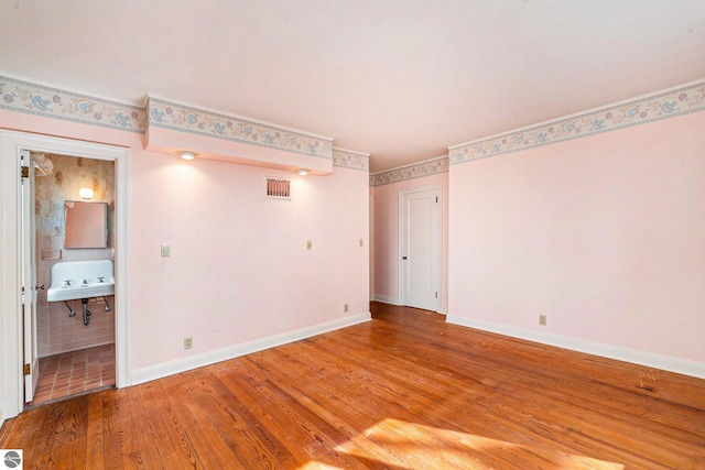 unfurnished room with a sink, visible vents, baseboards, and wood finished floors