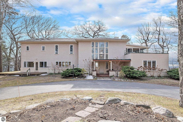back of house with stucco siding, a balcony, and aphalt driveway