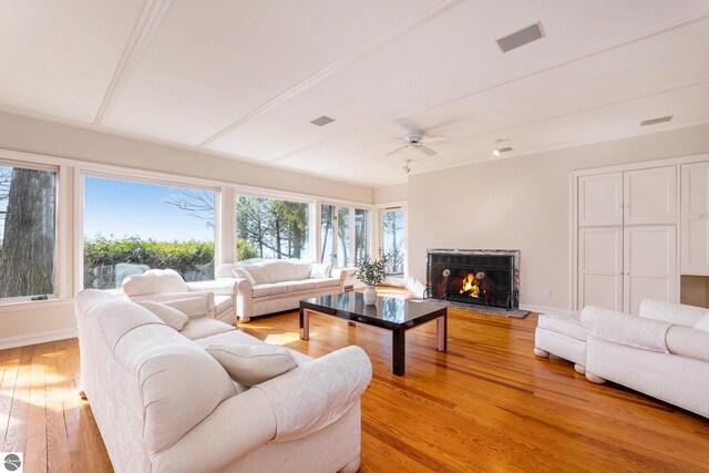living room with visible vents, baseboards, light wood-type flooring, a warm lit fireplace, and a ceiling fan