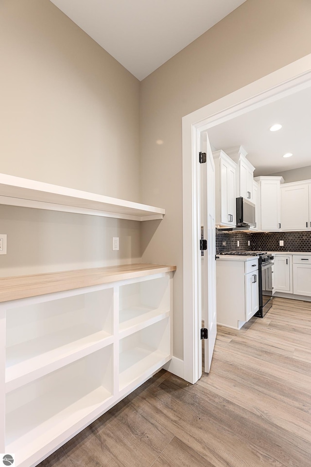 kitchen with light wood-style flooring, open shelves, tasteful backsplash, black gas stove, and white cabinets