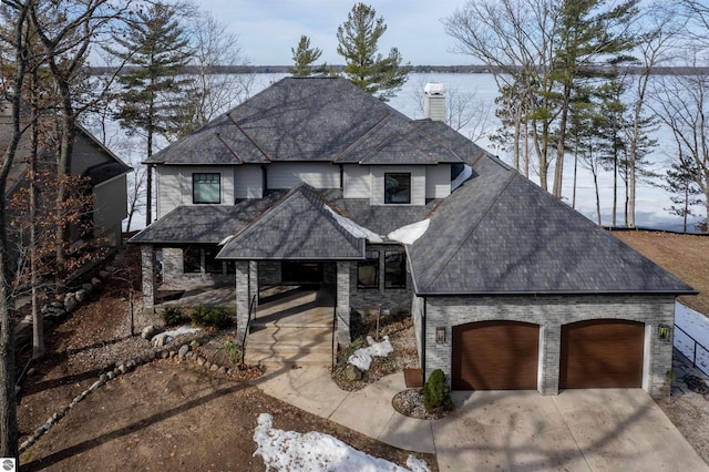 5568 Lakeview Dr, Interlochen, MI 49643 - view of front facade featuring a chimney, driveway, a water view, a garage, and a shingled roof