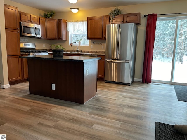 11893 Lillian Lee Dr, Interlochen, MI 49643 - kitchen with appliances with stainless steel finishes, a center island, a sink, light wood-type flooring, and dark countertops